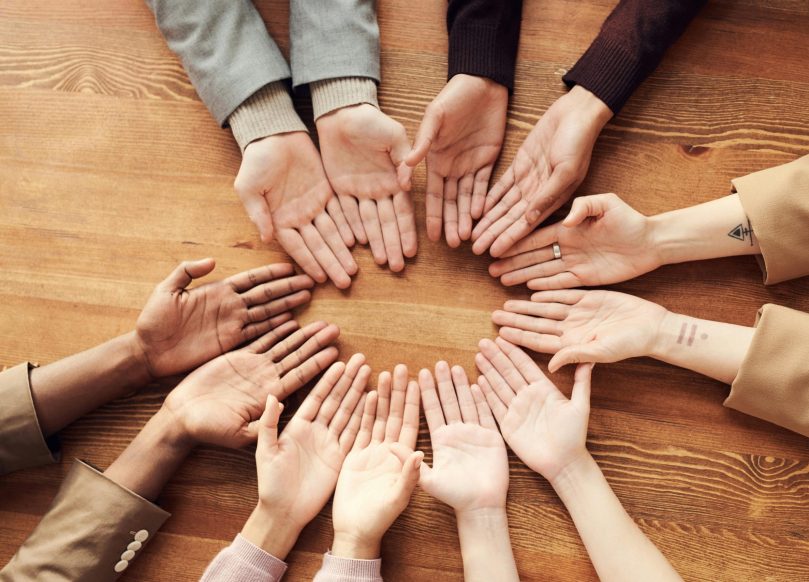 Multiple hands palms-up in a circle from people of different races.