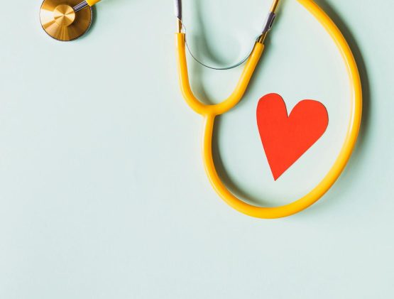 Yellow stethoscope on a light blue background. Red heart inside the loop of the stethoscope.