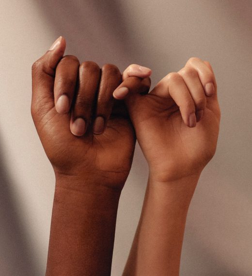 Two hands rise up over a taupe background in Pinky Promise position