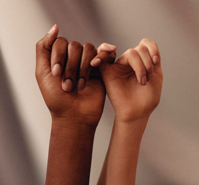 Two hands rise up over a taupe background in Pinky Promise position